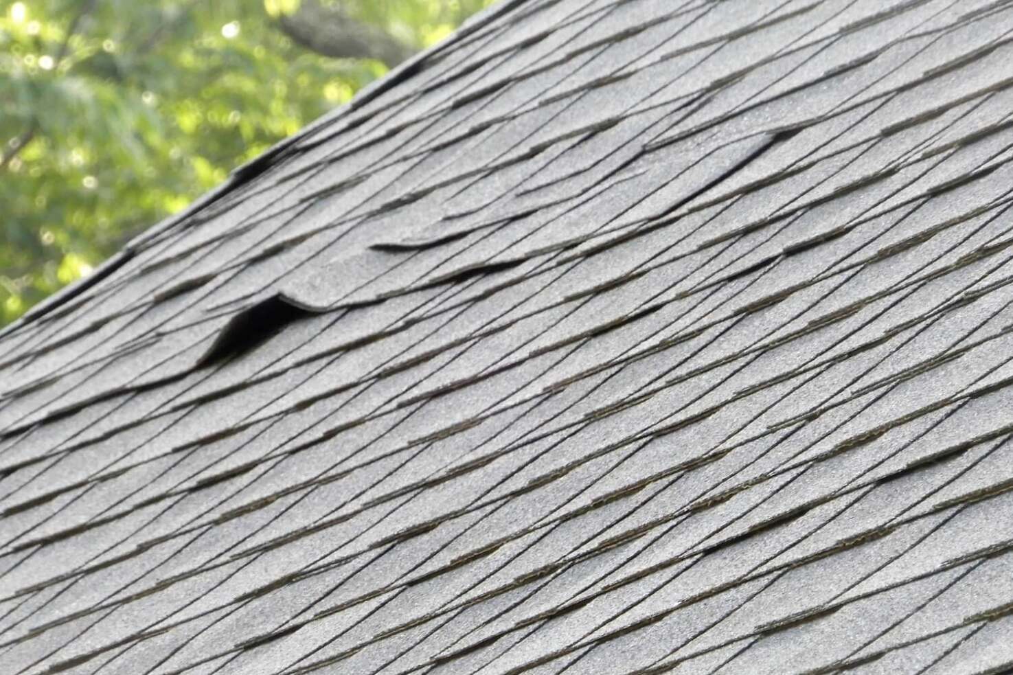 A photo showing a close-up view of buckled shingles on a roof