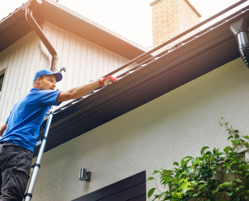 Roofing contractor cleaning out gutters by hand